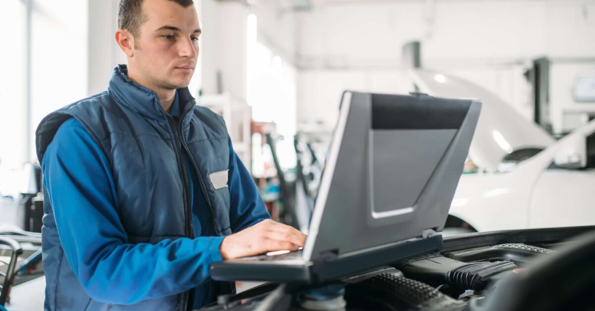 Man at auto dealership on a laptop on top of a car engine